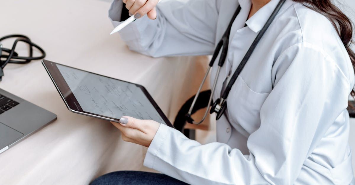 A doctor is sitting at a table holding a tablet and a pen.