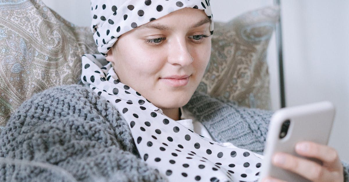 A woman with cancer is sitting on a couch looking at her cell phone.