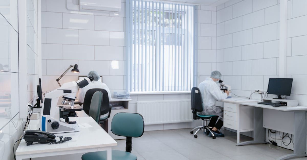 A man is sitting at a desk in a lab looking through a microscope.