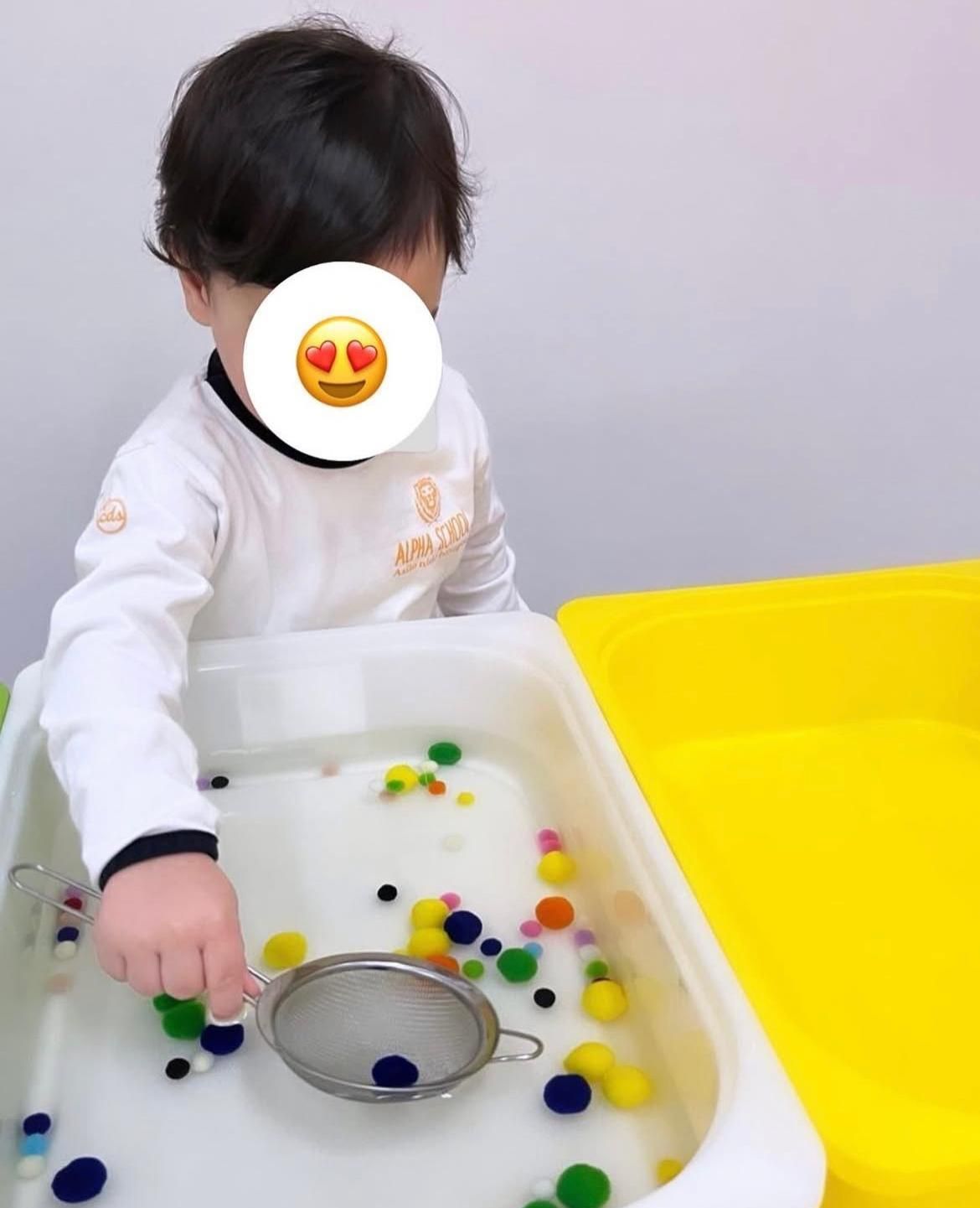 Un bambino che gioca con un colino in una vaschetta d'acqua