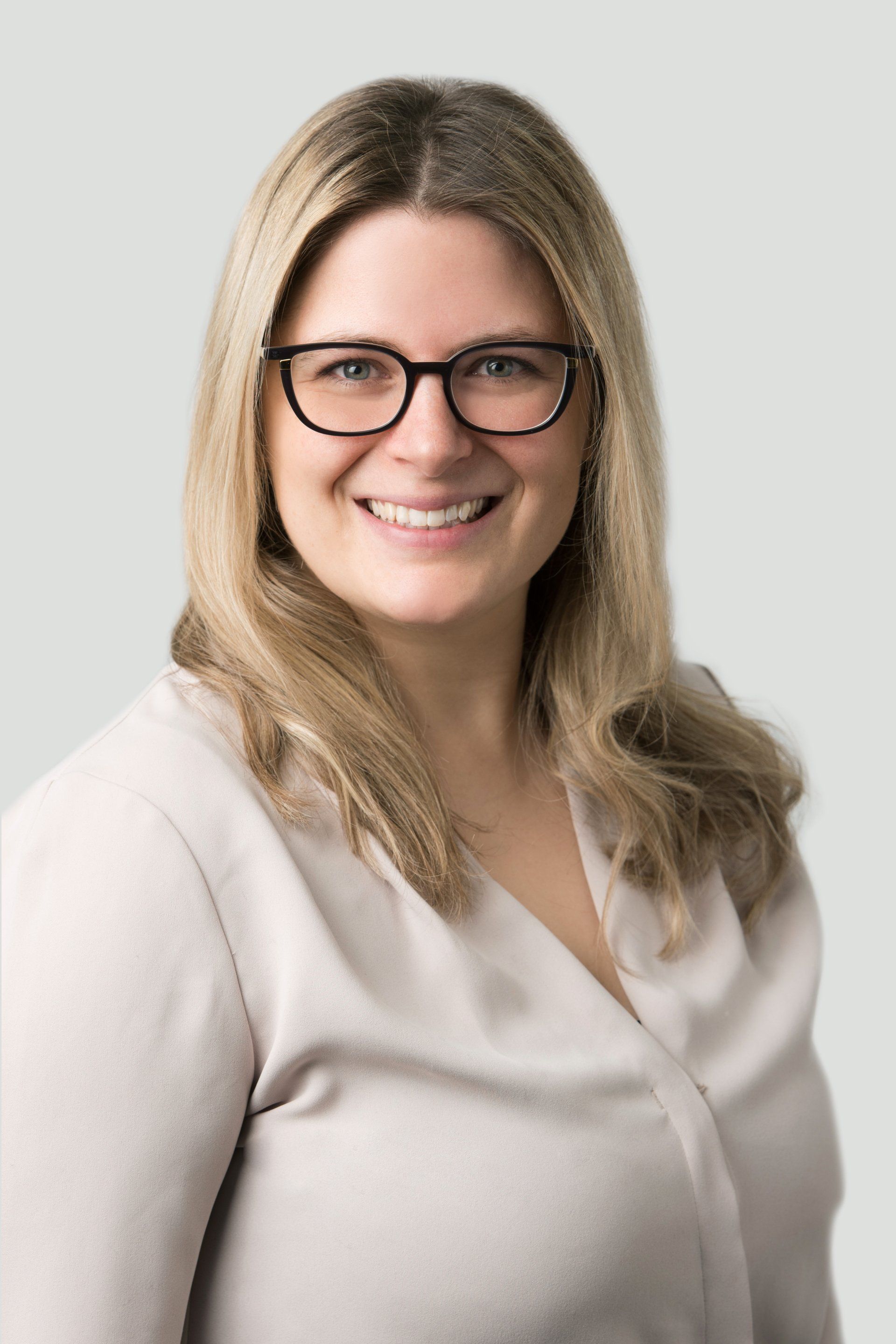 A woman wearing glasses and a white shirt is smiling for the camera.