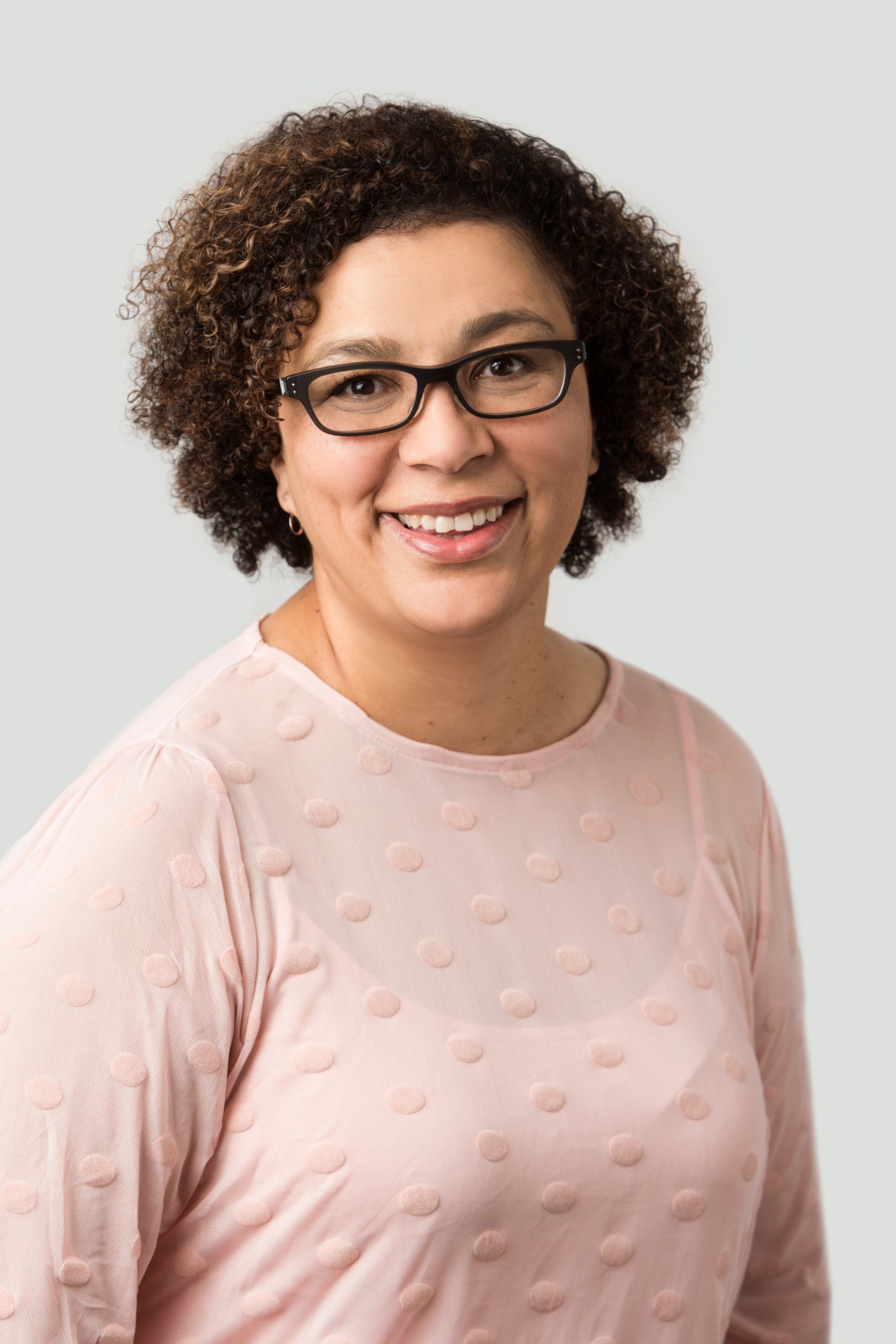 A woman wearing glasses and a pink shirt is smiling for the camera.