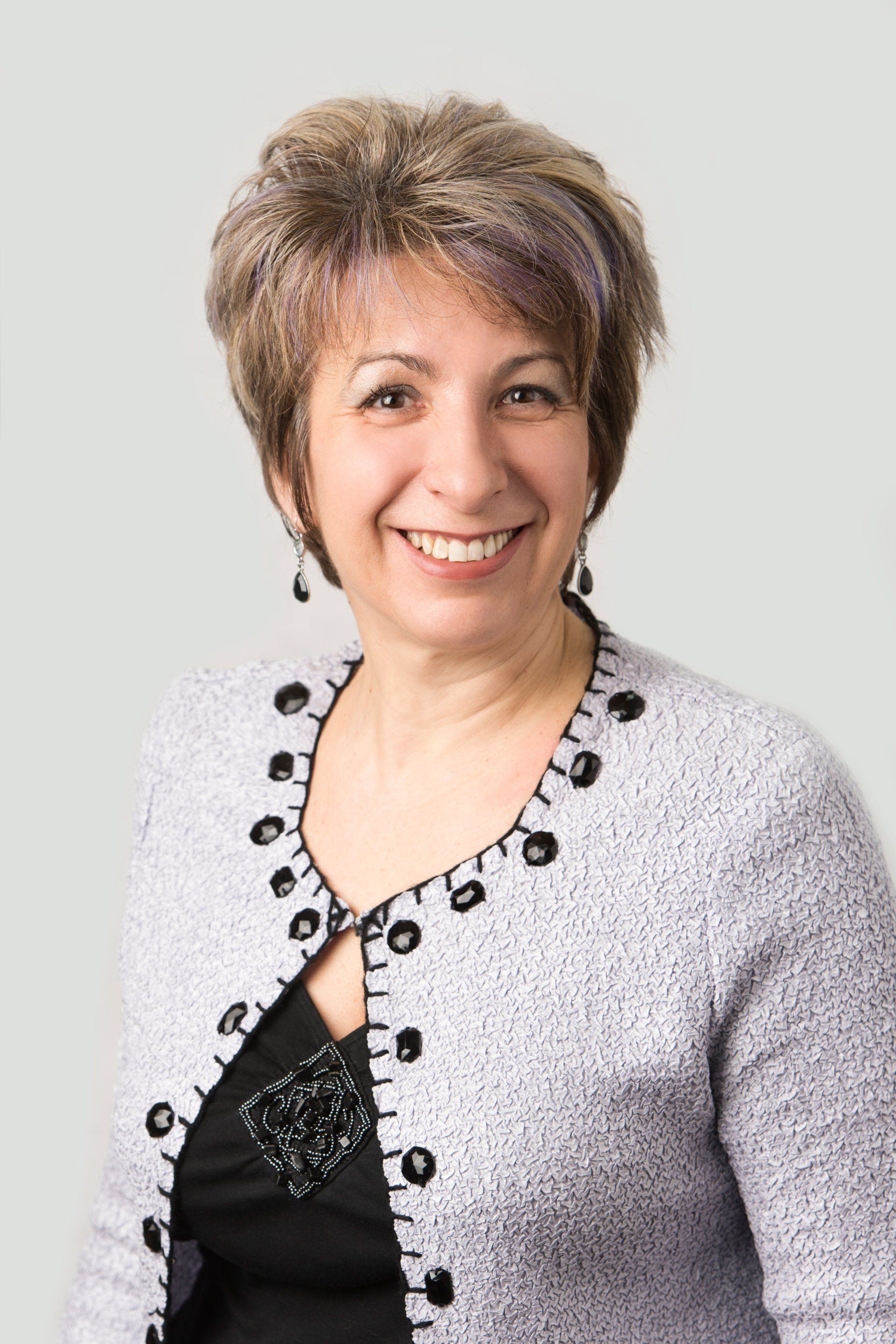 A woman wearing a gray sweater and a black shirt is smiling for the camera.