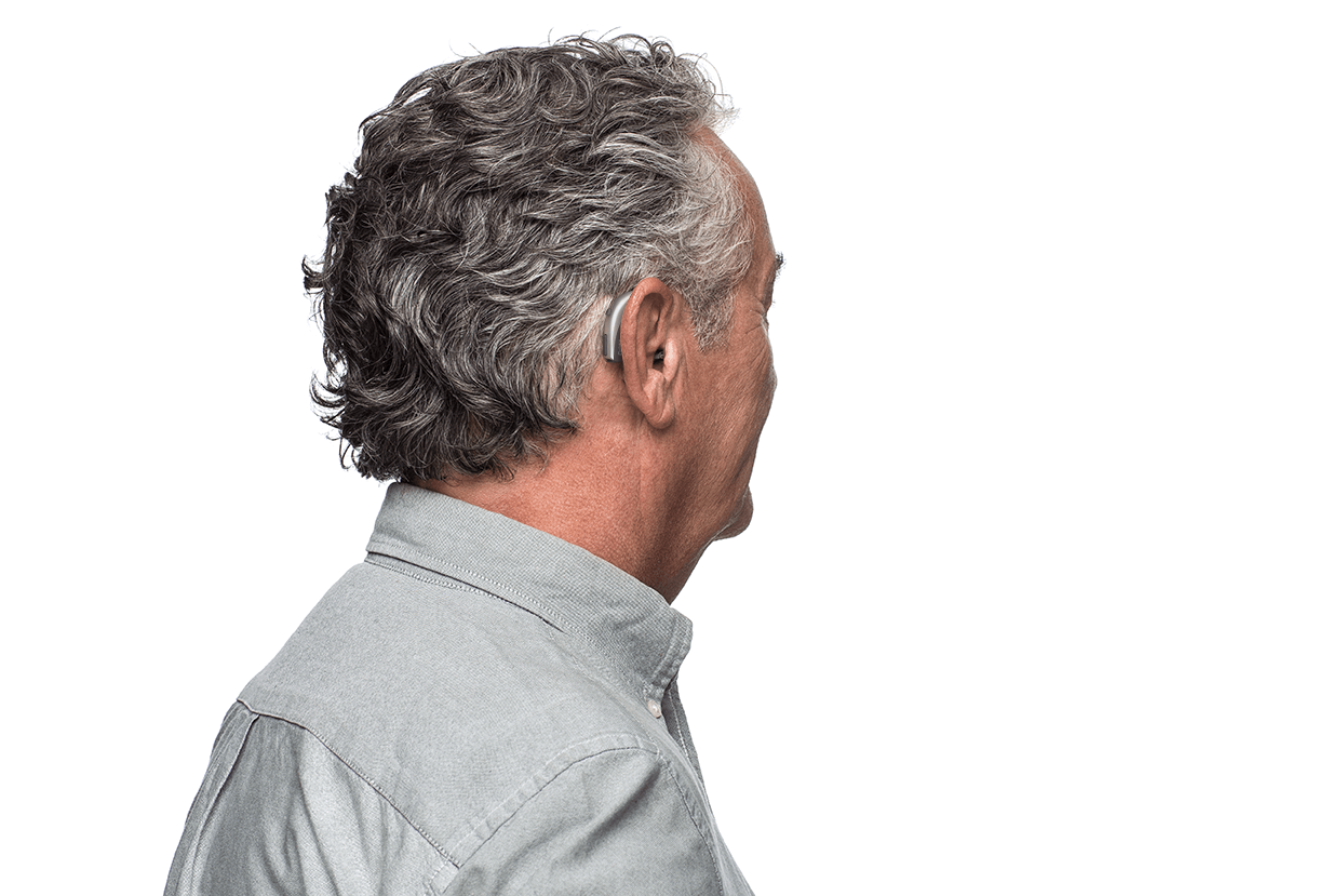 A man wearing a hearing aid is standing in front of a white background.