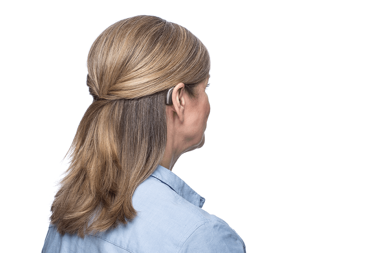 A woman wearing a hearing aid is standing in front of a white background.