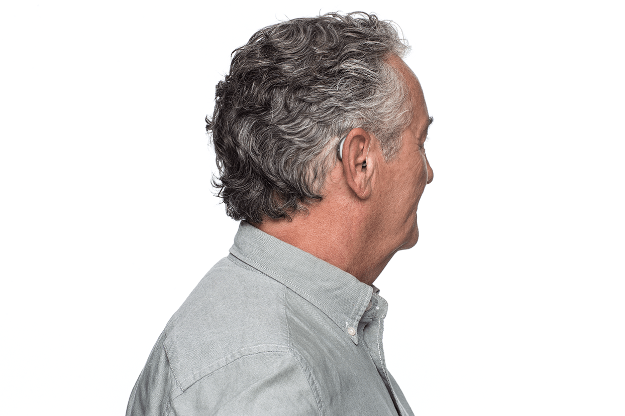 A man wearing a hearing aid is standing in front of a white background.