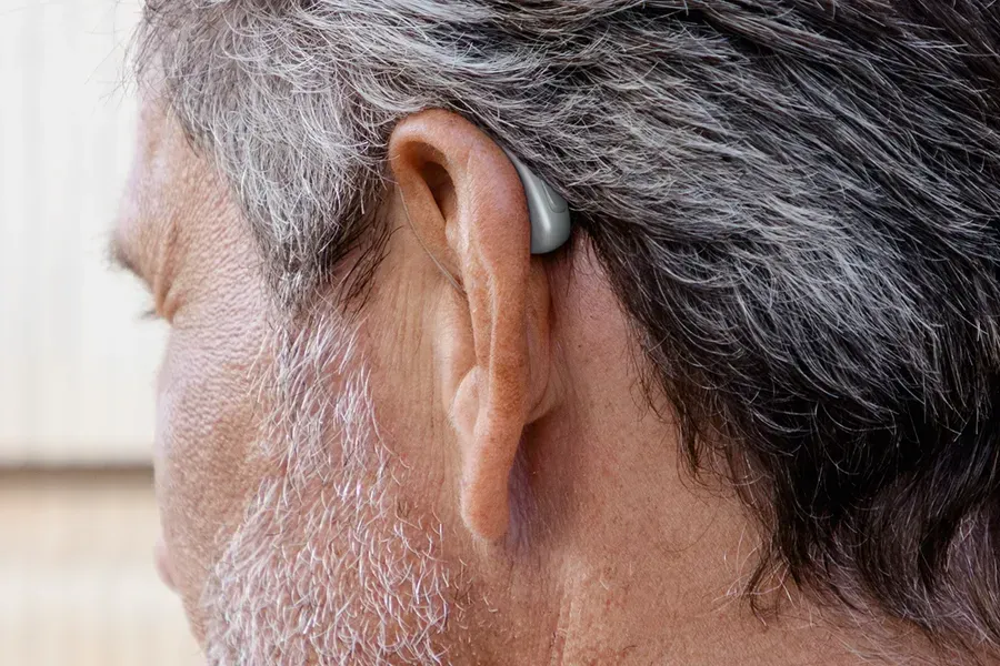 A man with a beard is wearing a hearing aid in his left ear.