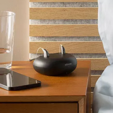 A pair of hearing aids are sitting on a wooden nightstand next to a glass of water.