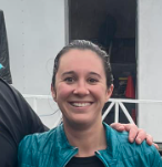 Man in green polo stands on a football field, arms crossed, stadium in background.