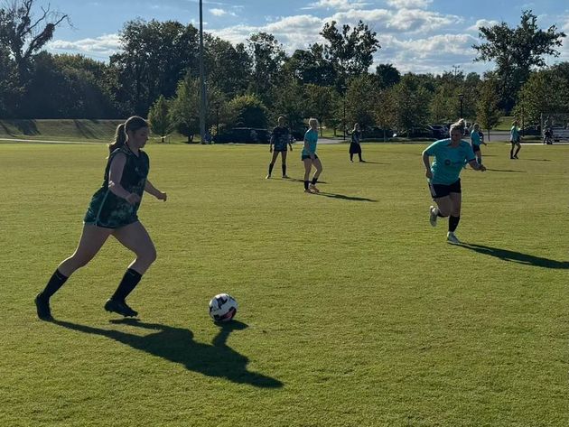 Baseball glove with ball on green grass, with blurred baseballs in the background.