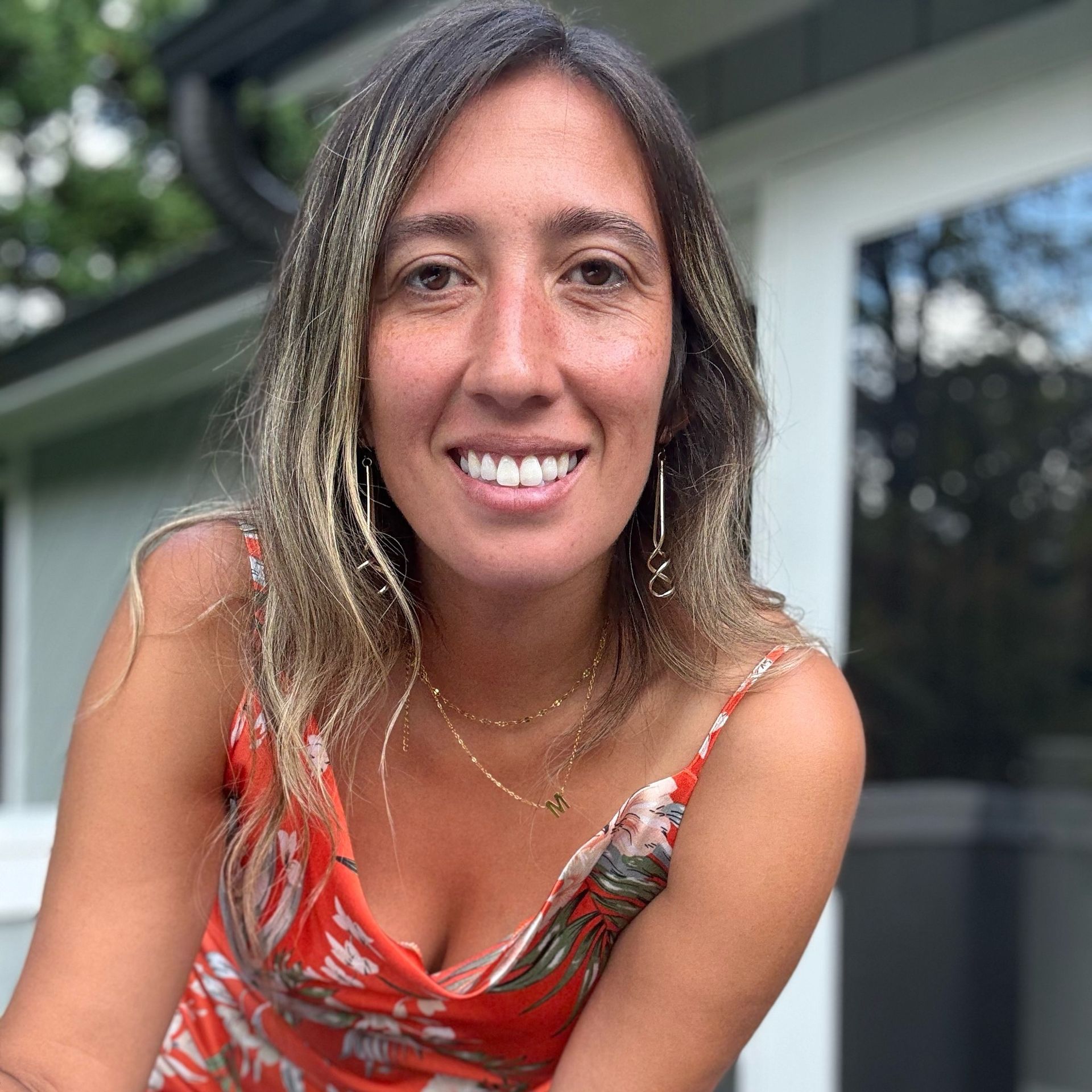 Football coach with arms crossed, standing on a football field. He wears a navy polo shirt and gray pants.