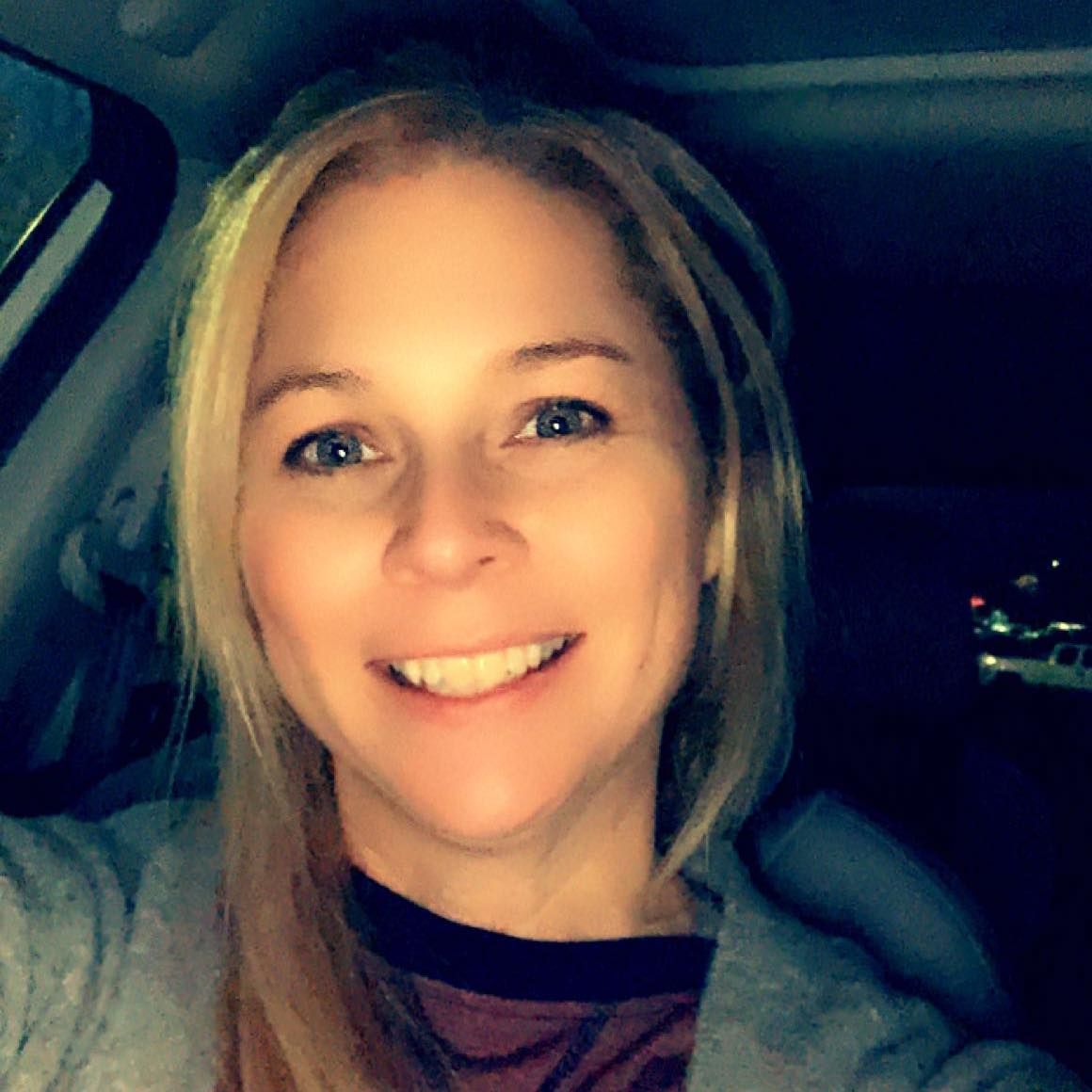 Football coach with arms crossed, standing on a football field. He wears a navy polo shirt and gray pants.
