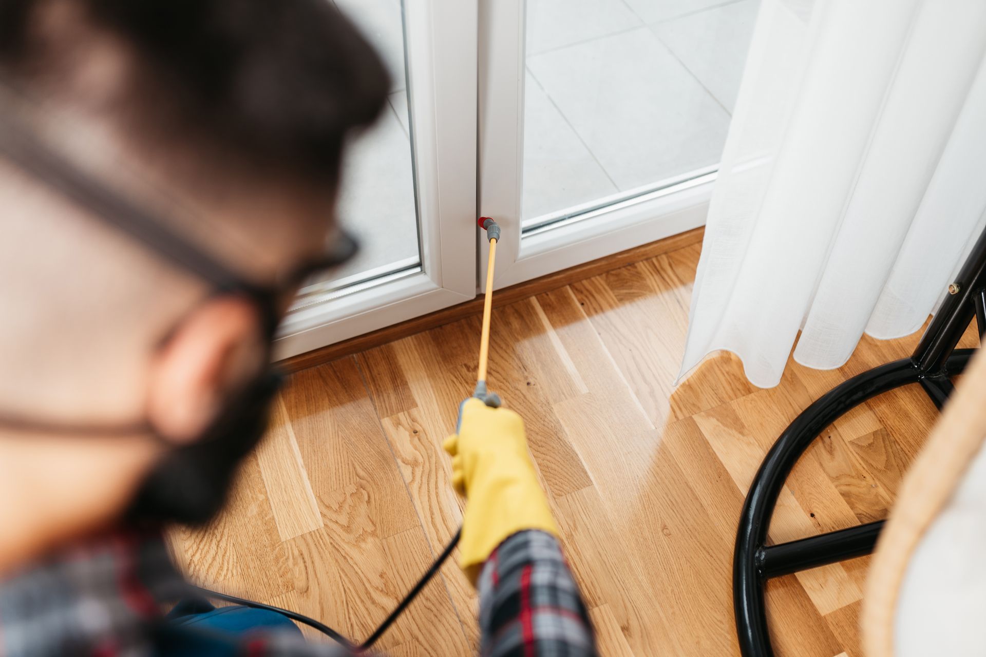 A man wearing a mask and gloves is spraying a chemical on a wooden floor.