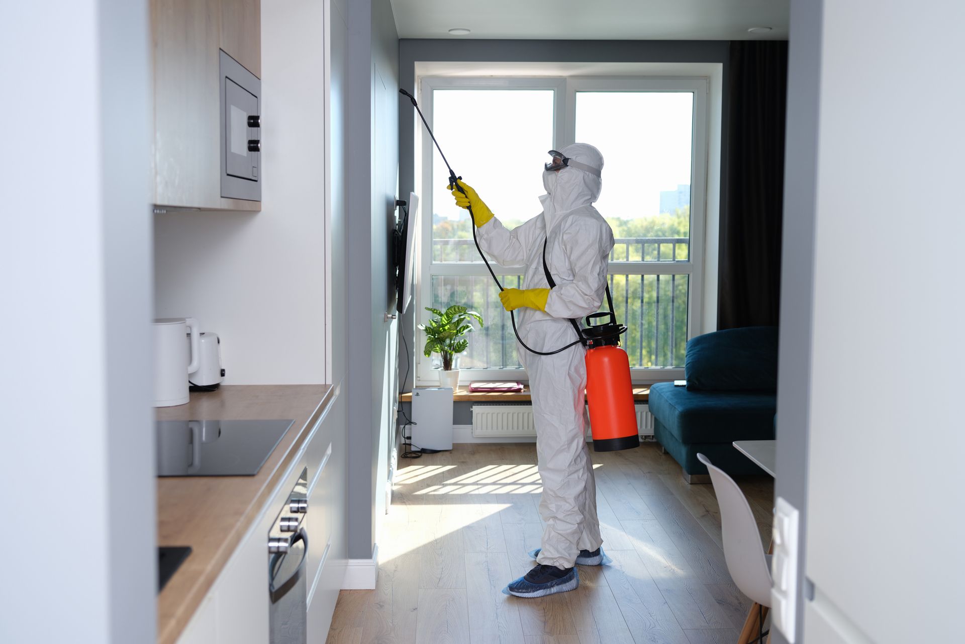 A man in a protective suit is spraying a room with a sprayer.