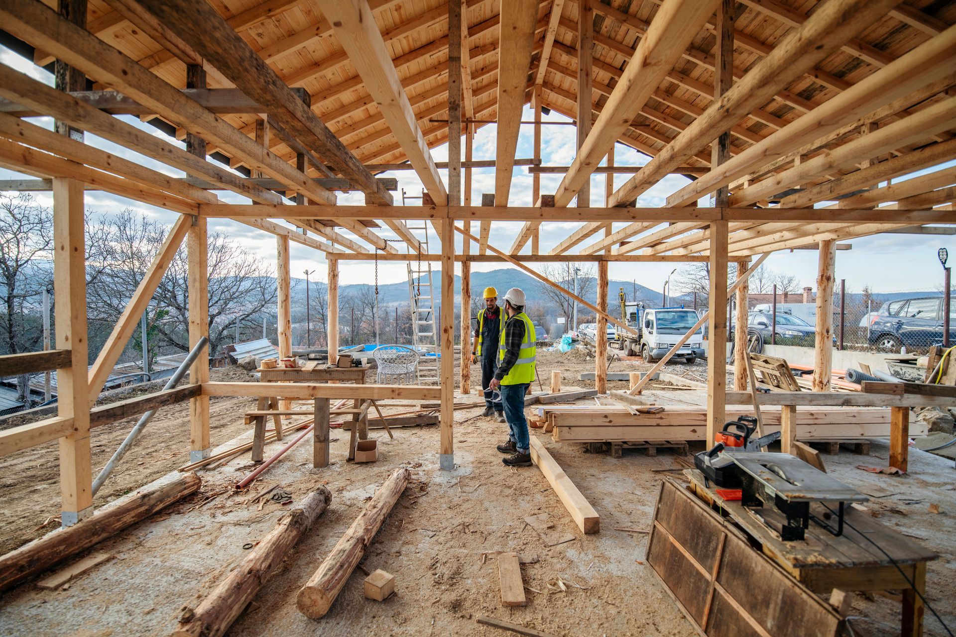 Two construction workers are standing inside of a wooden structure under construction.