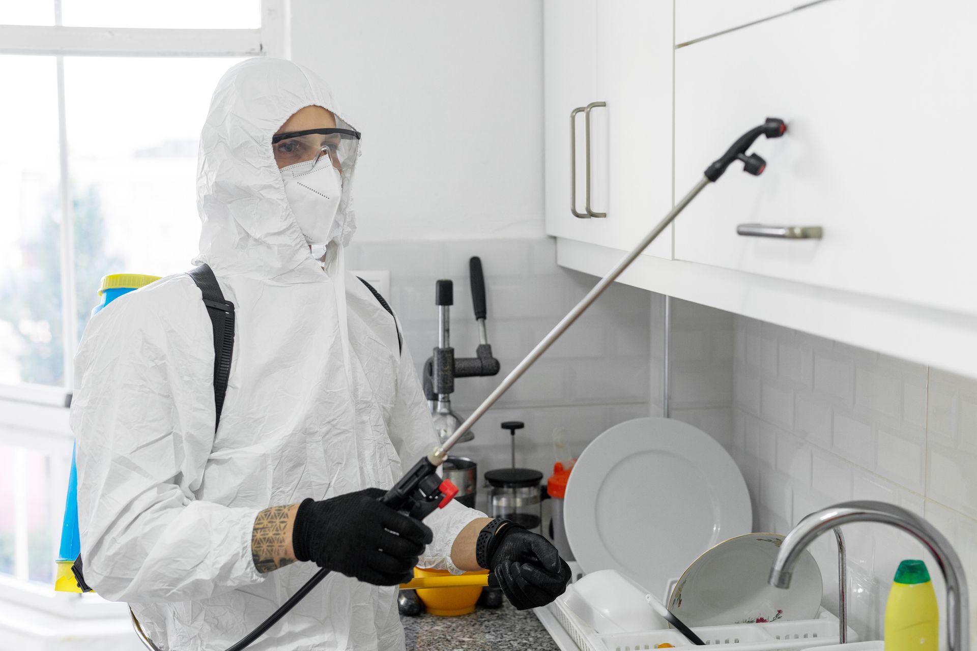 A man in a protective suit is spraying a kitchen counter with a sprayer.