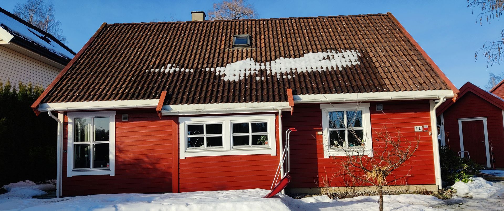 Et rødt hus med brunt tak og hvite vinduer er dekket av snø.