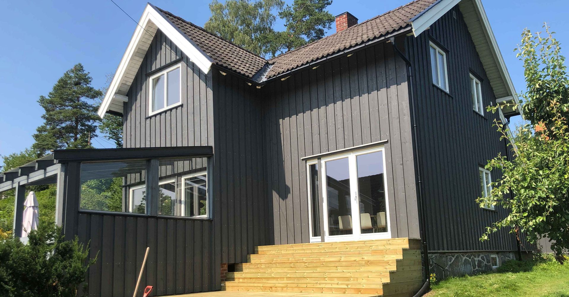 Et svart hus med en treterrasse og trapp som fører opp til det.