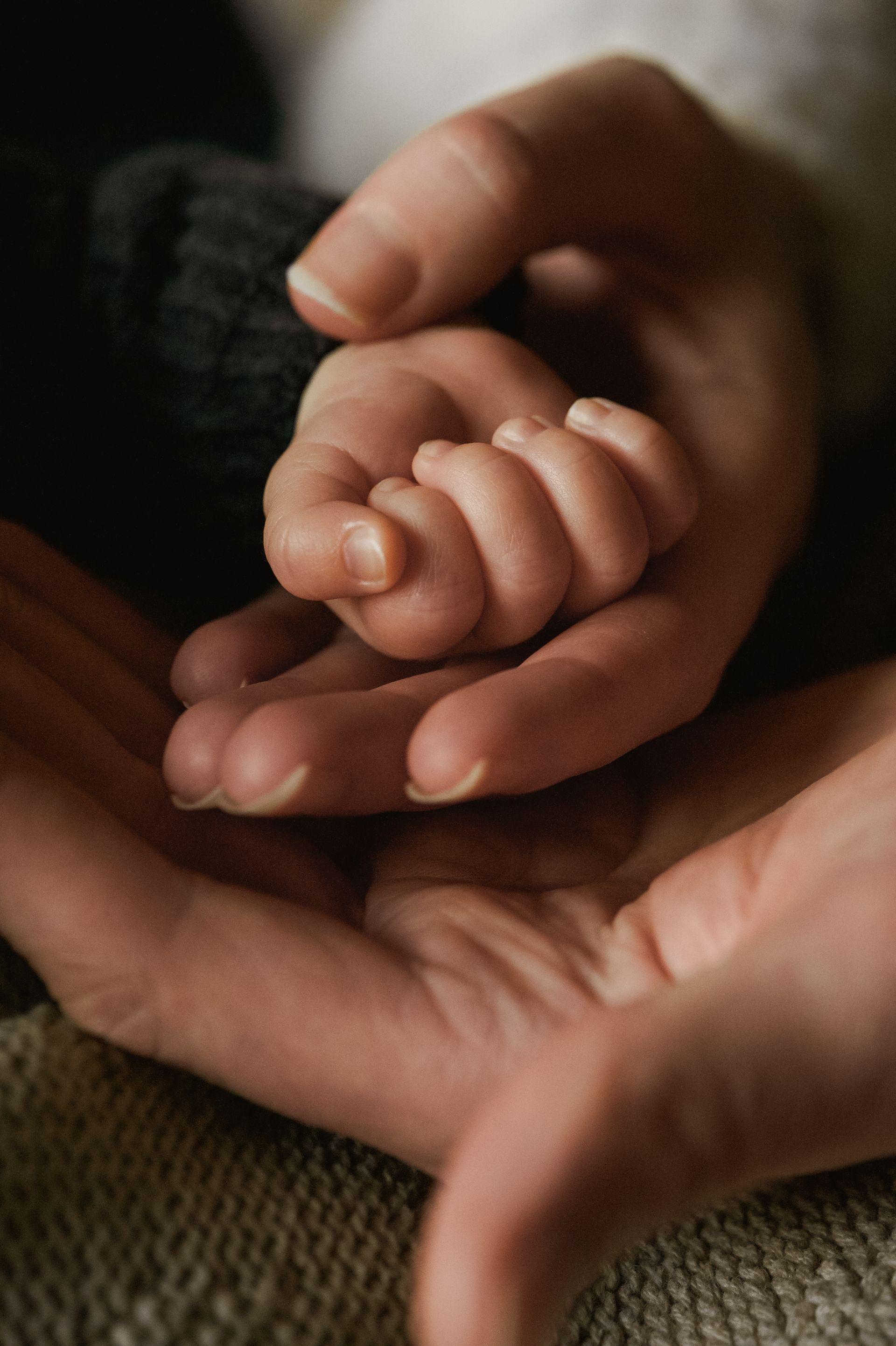 Volwassen handen die het kleine handje van een baby  teder omvatten.