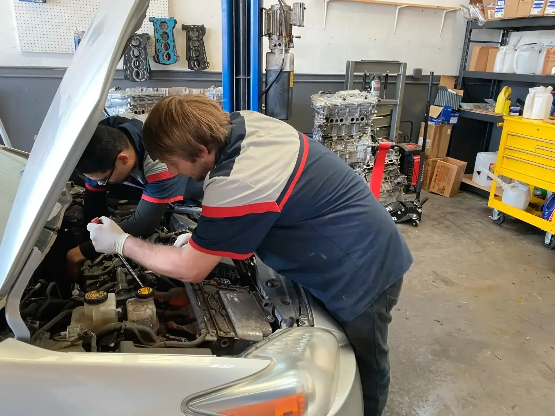 Two mechanics work under an open car hood in a repair shop