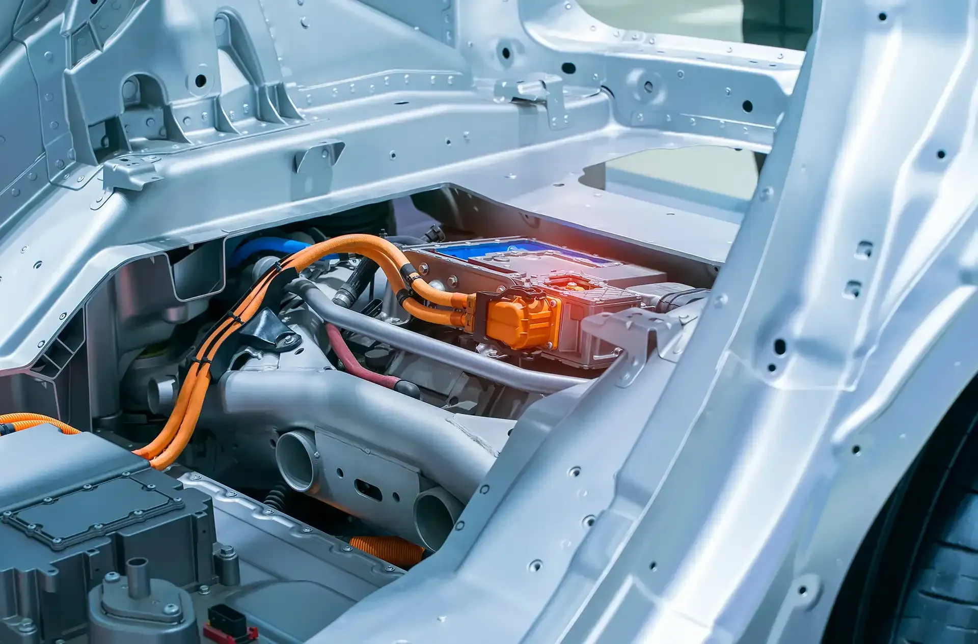Car chassis interior with exposed wiring, metal frame, and orange cables in a factory setting