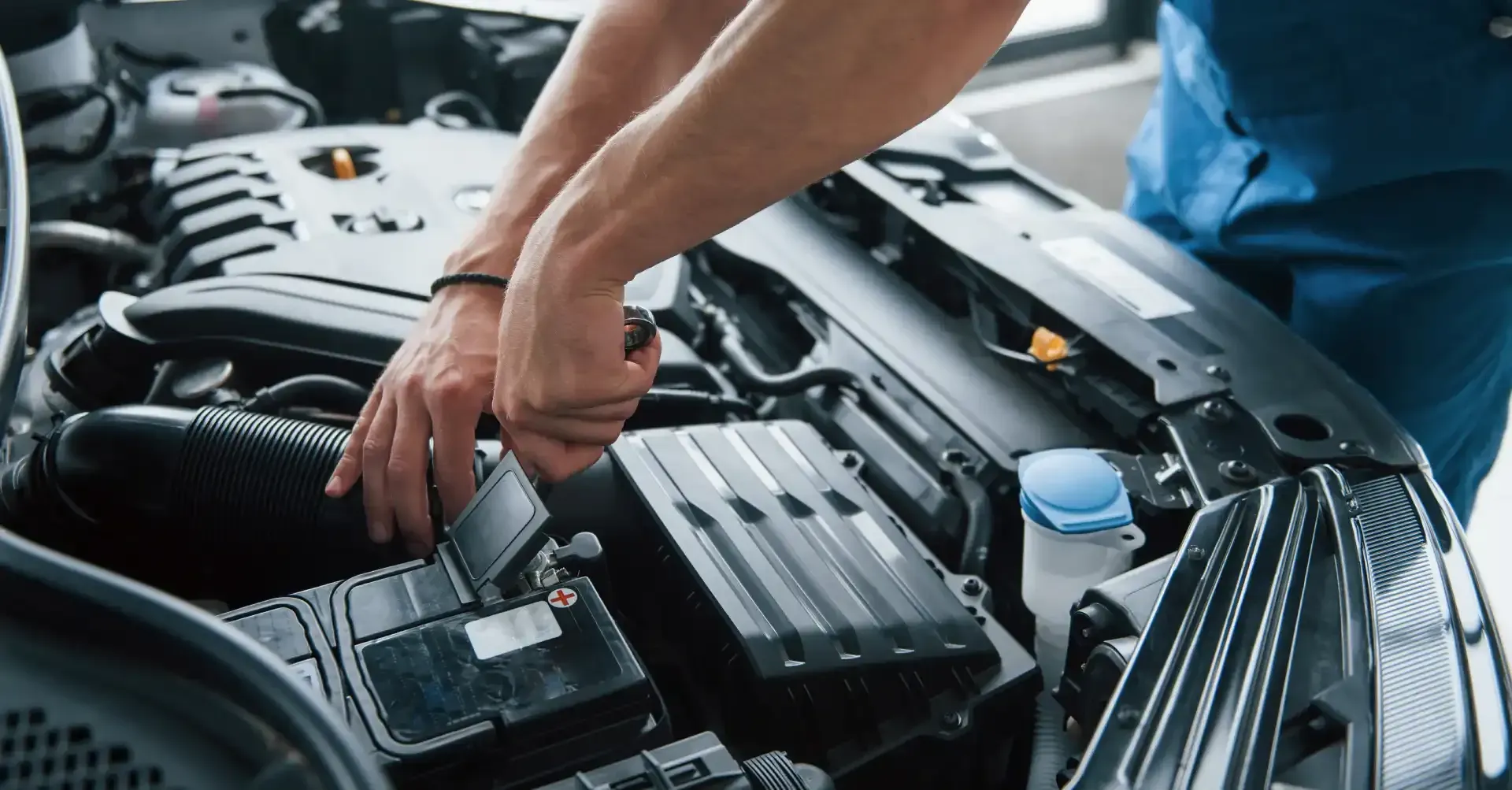 Mechanic checking a car battery and engine components under an open hood
