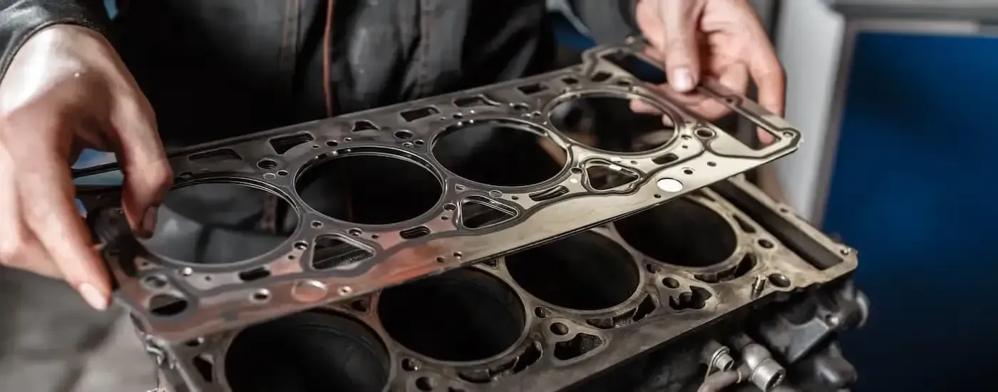 Hands holding two stacked car engine head gaskets in a workshop