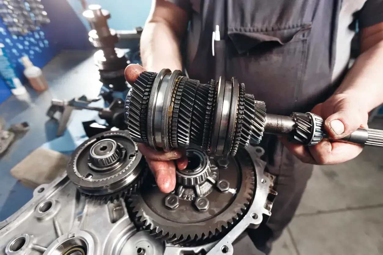 Mechanic holding a disassembled metal gearbox and gears in a workshop