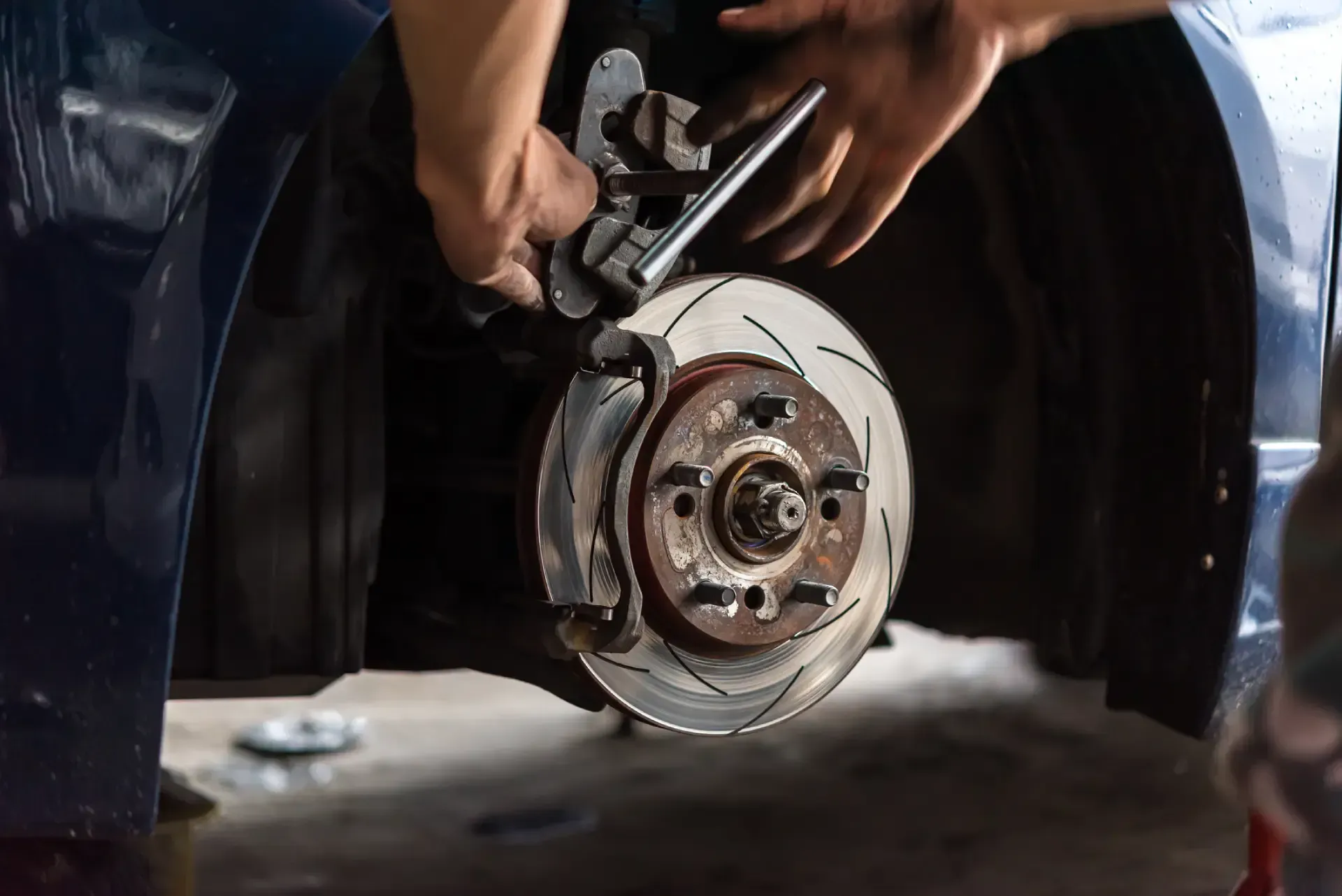 Hands using a brake tool to repair a car’s exposed wheel hub and brake rotor