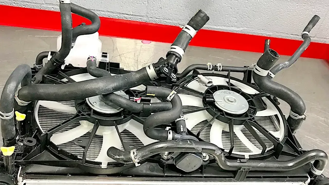 Black cables and hoses coiled in a tray with red and silver fittings against a light wall.