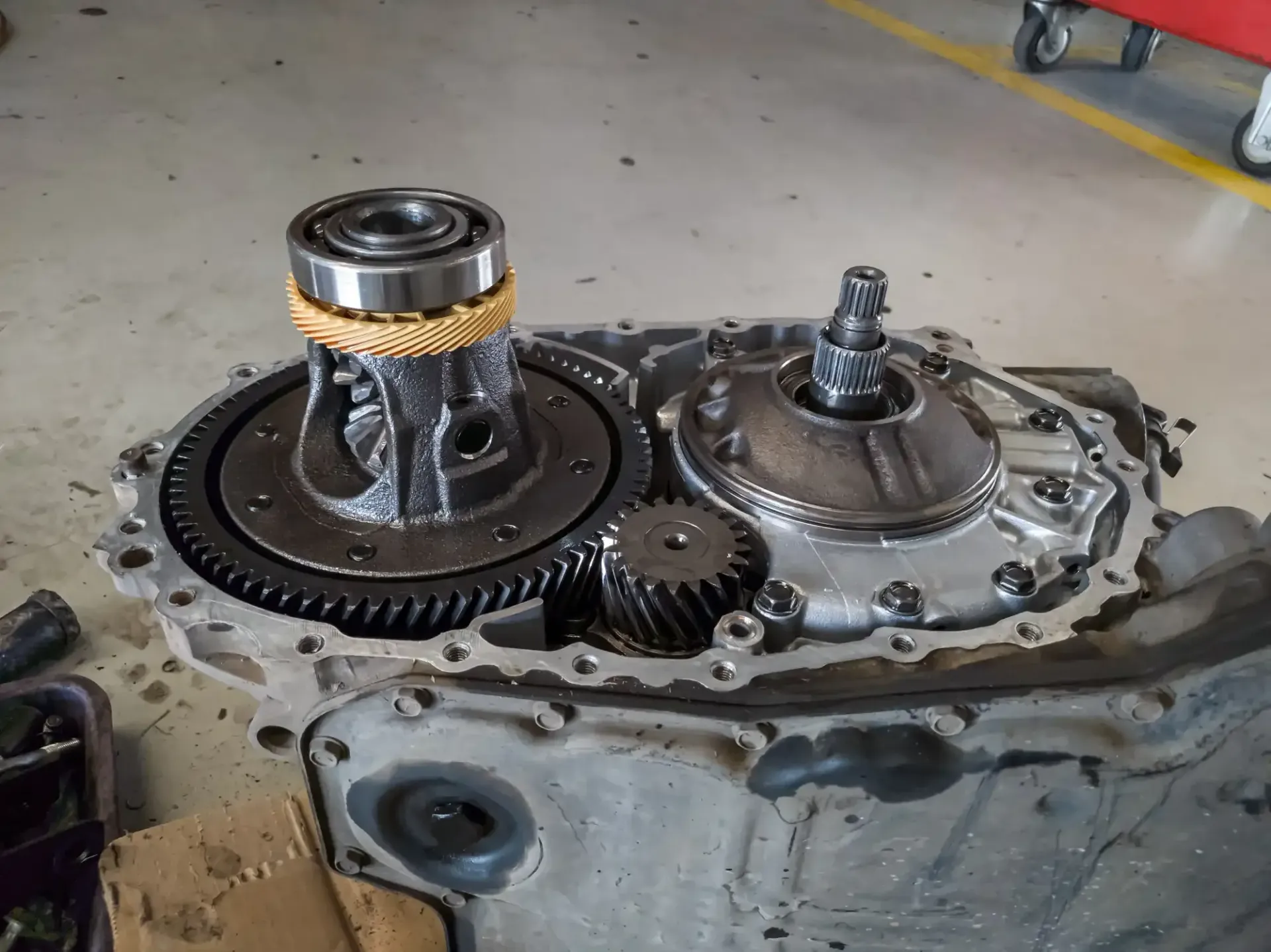 Open car transmission case with exposed gears and clutch components on a workshop floor