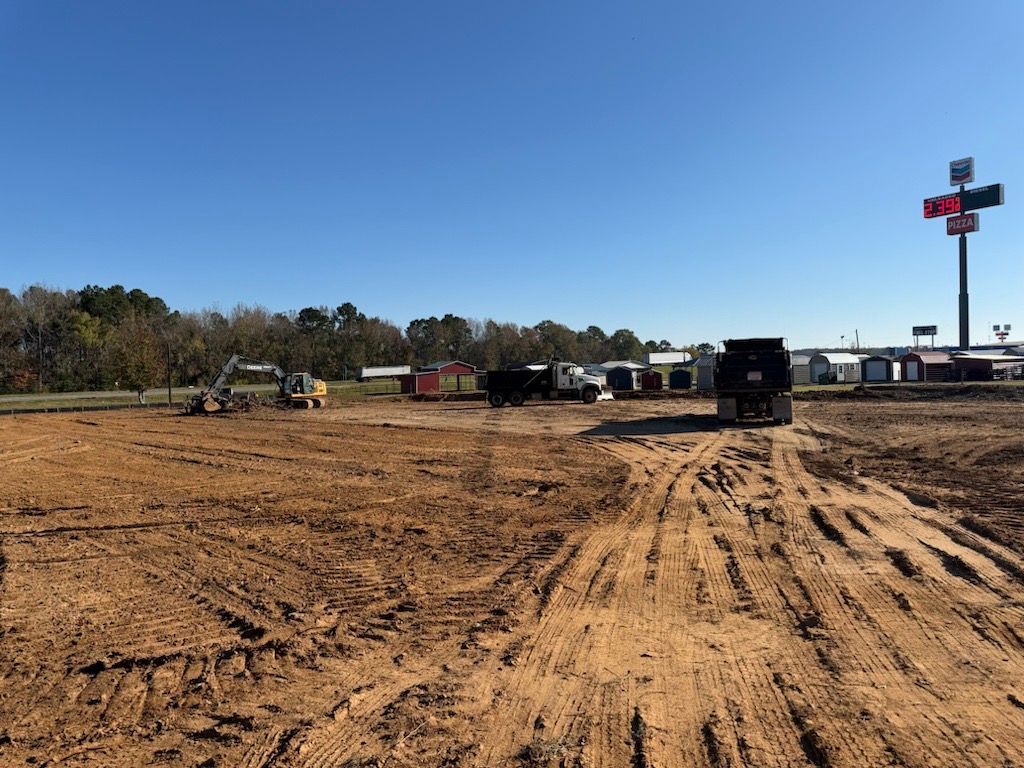 Construction site with heavy machinery, clear sky, and business sign in the background.