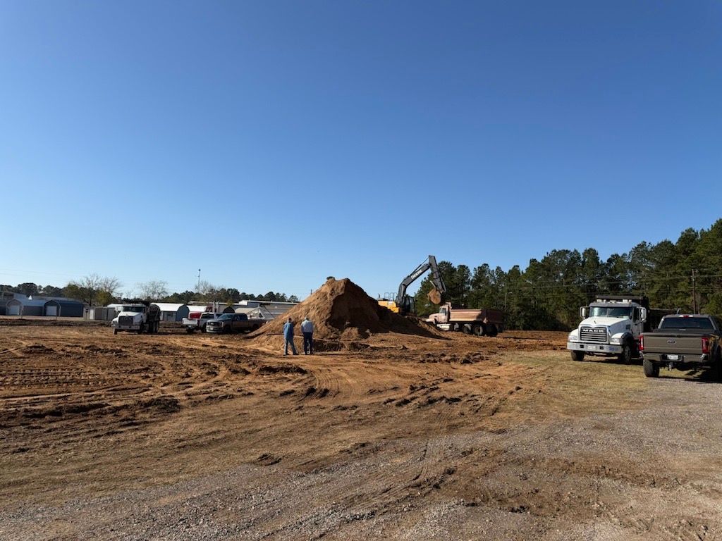 Construction site with earthmovers, trucks, and two people. Brown dirt under a clear blue sky.