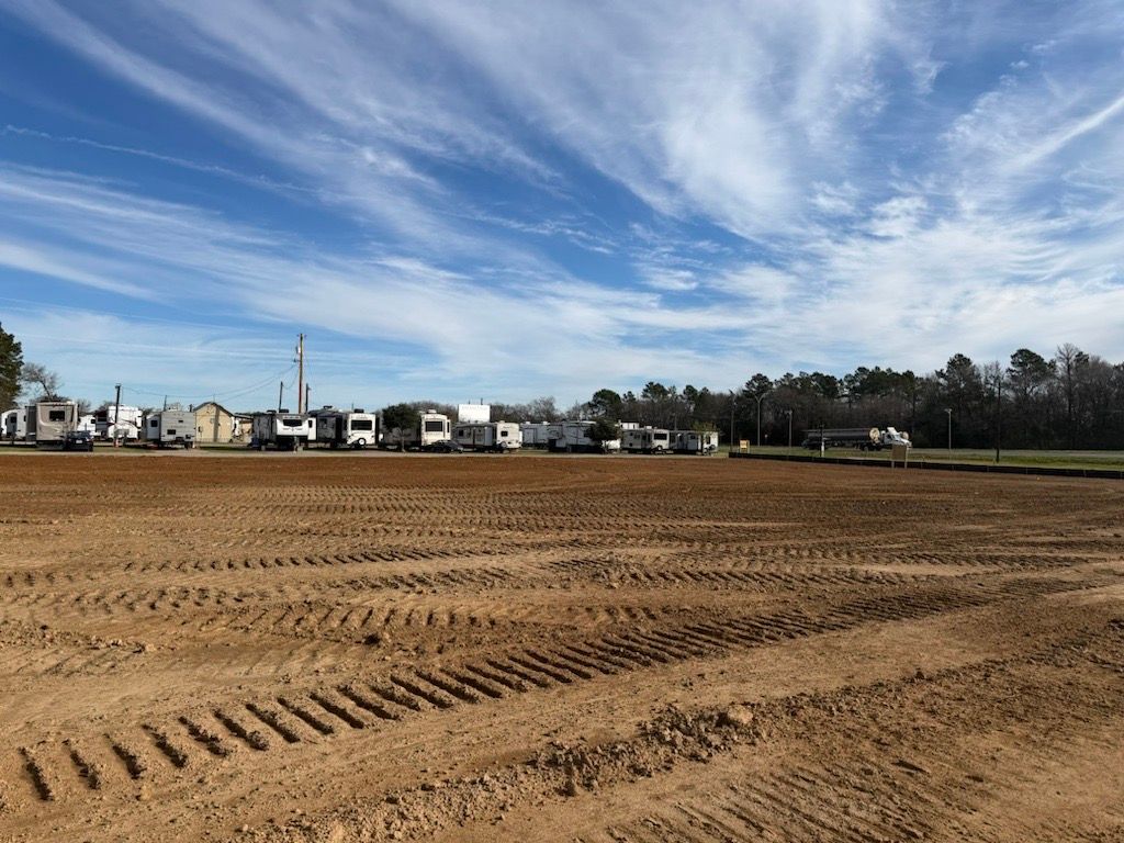 RV park with parked RVs on the horizon, foreground of freshly tilled dirt under a blue, cloudy sky.