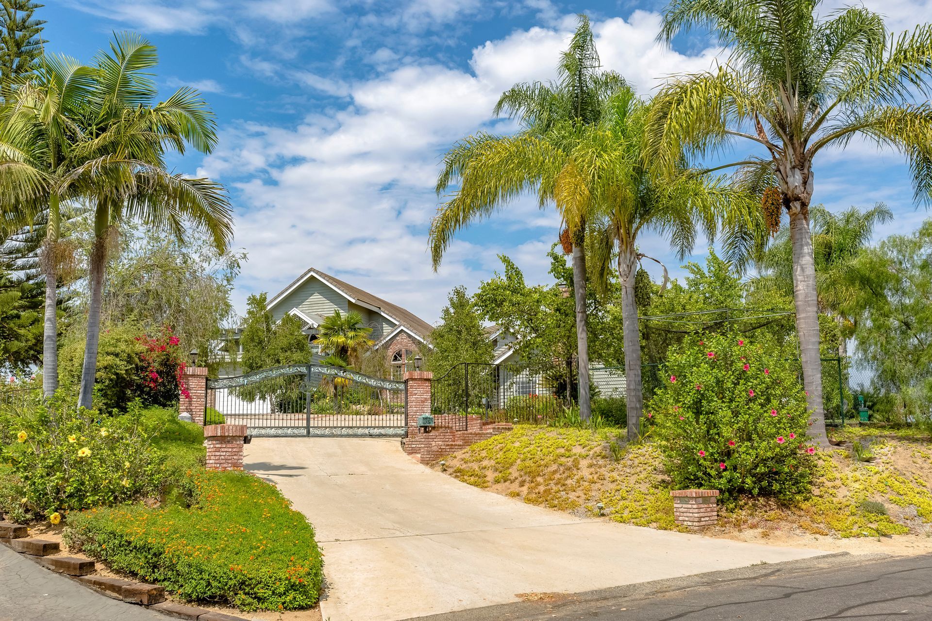 California home with gate below puffy clouds.