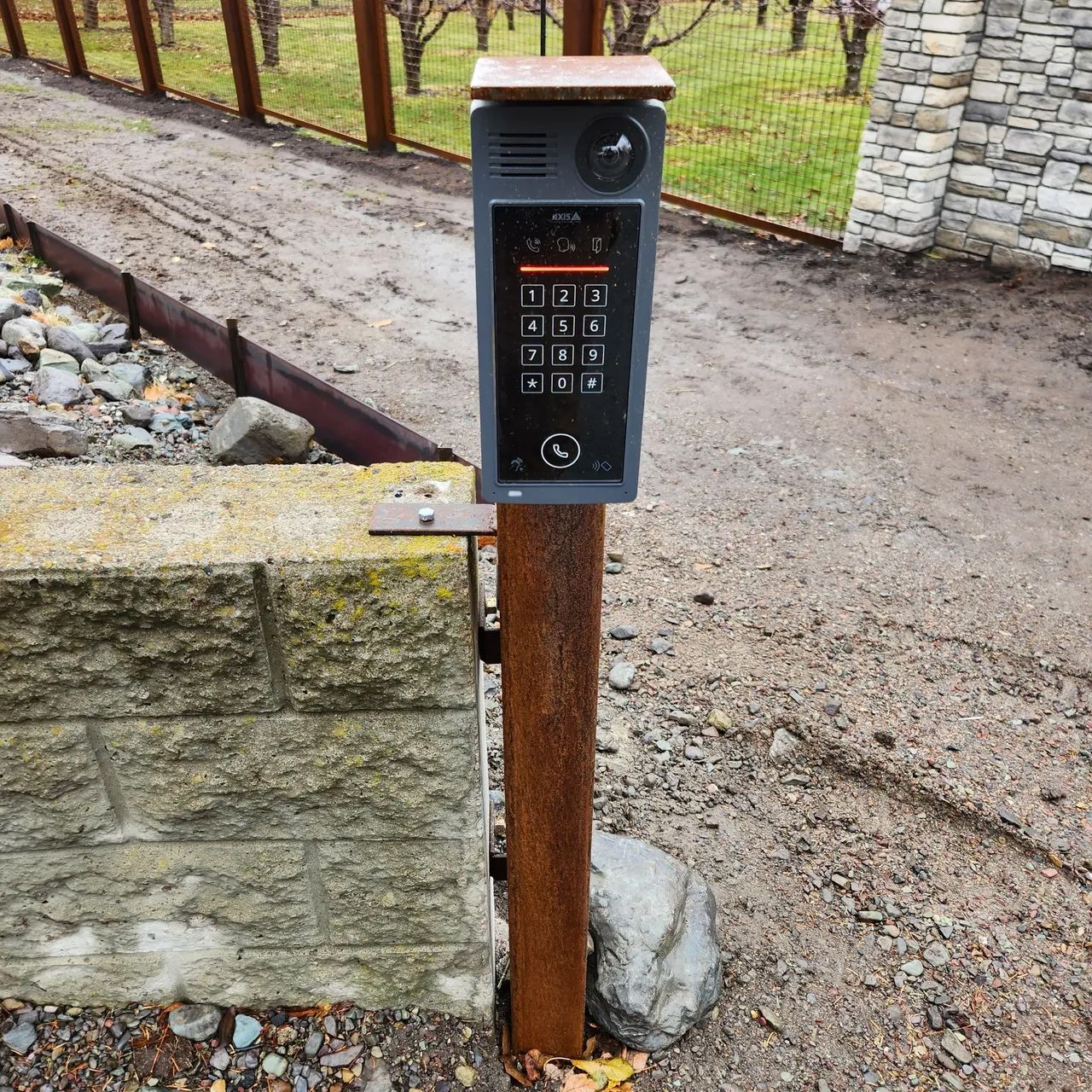 A keypad on a wooden post with a brick wall in the background