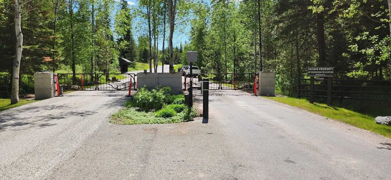 A gravel road with a gate in the middle of it surrounded by trees.