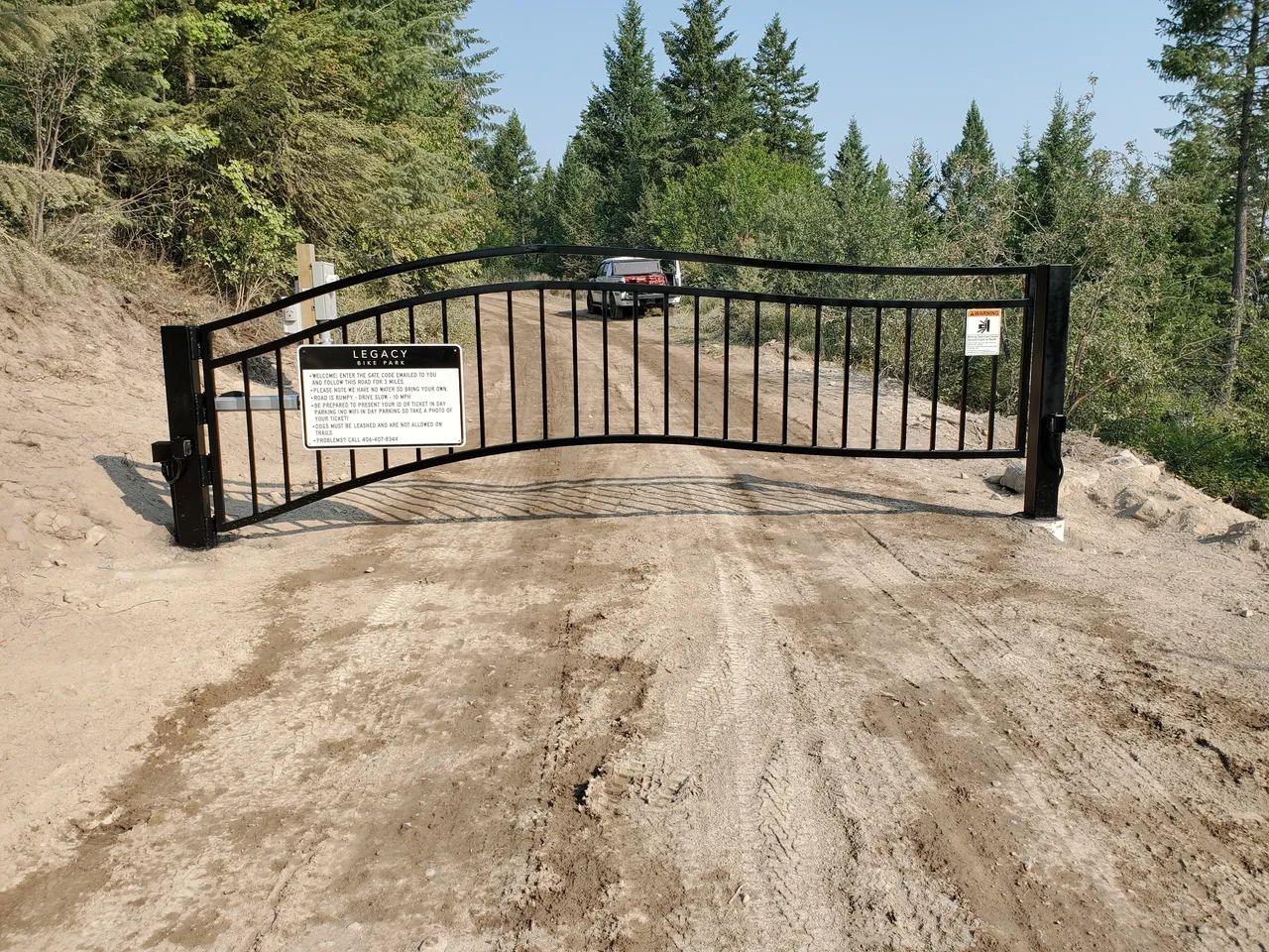 A metal gate is sitting on the side of a dirt road.