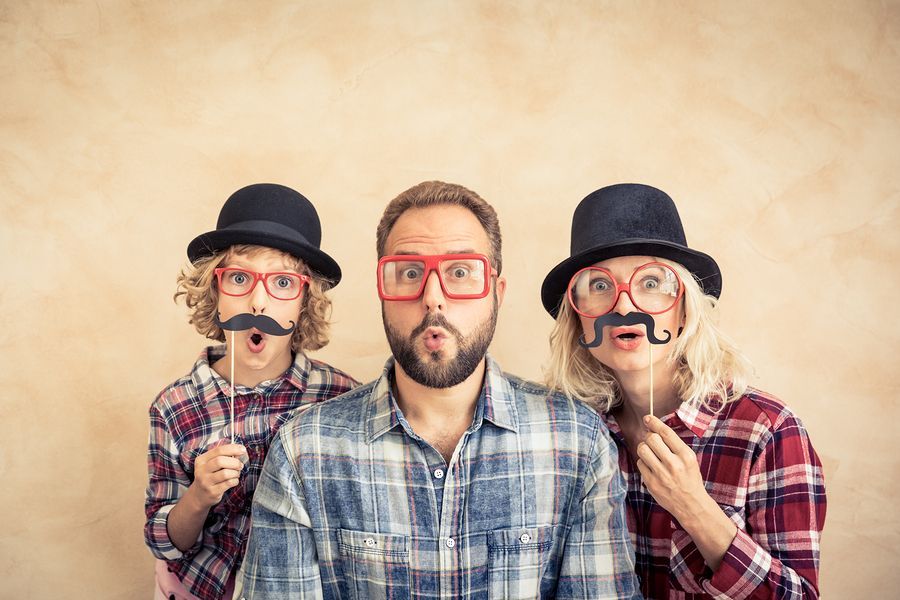 Family wearing props of hats, mustaches, and glasses, making surprised faces.