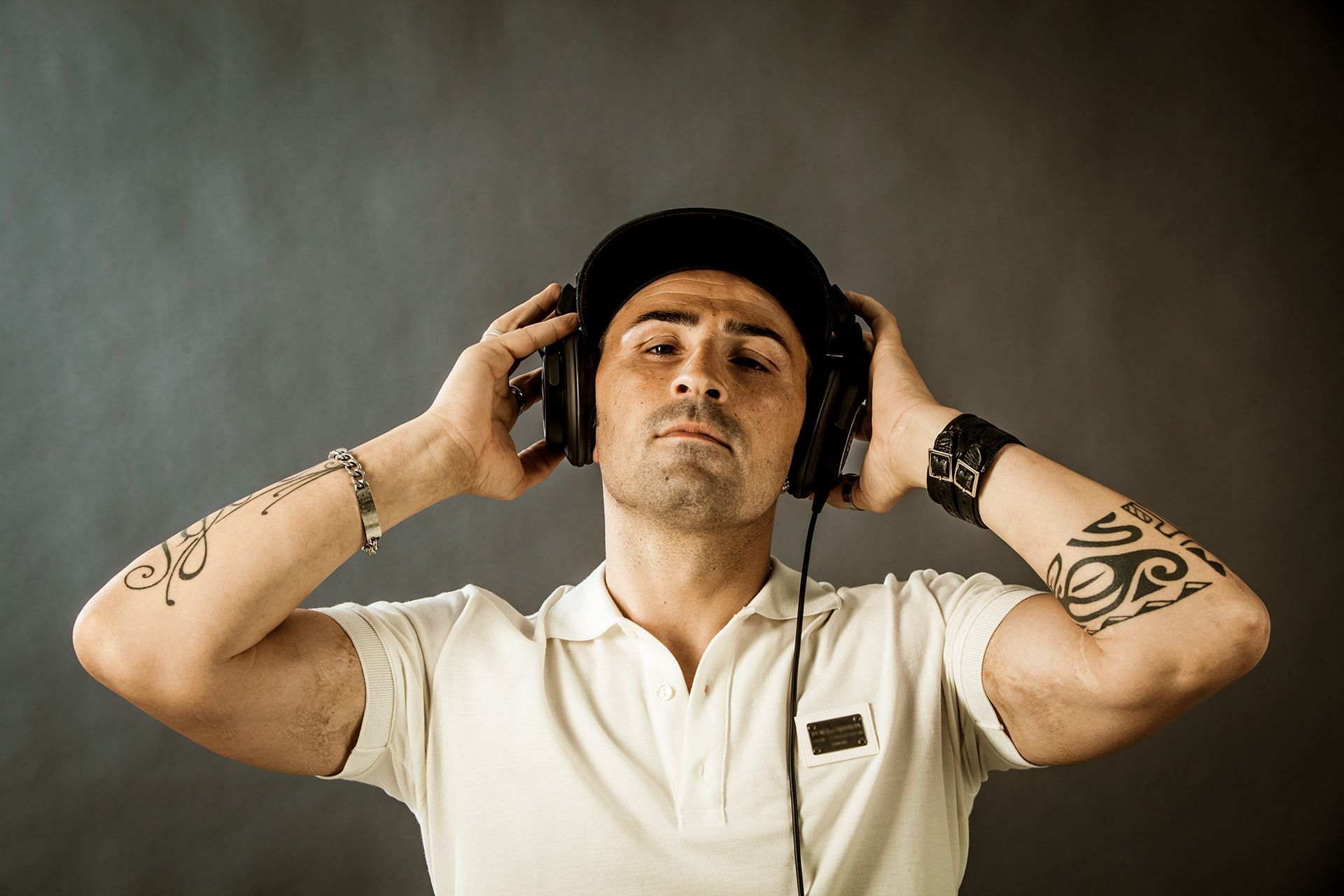 Man wearing headphones and a baseball cap, listening to music, against a gray backdrop.