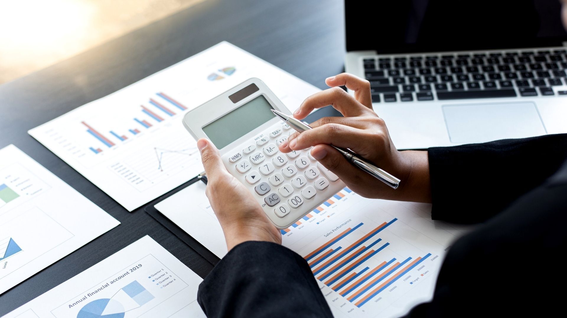 A woman is using a calculator in front of a laptop computer.