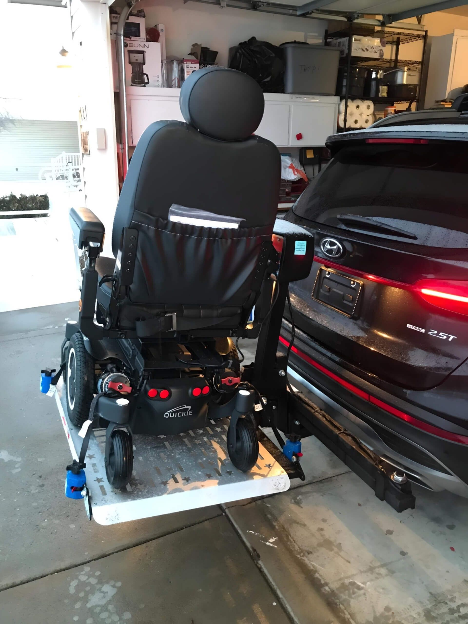 A wheelchair is attached to the back of a black car in a garage.