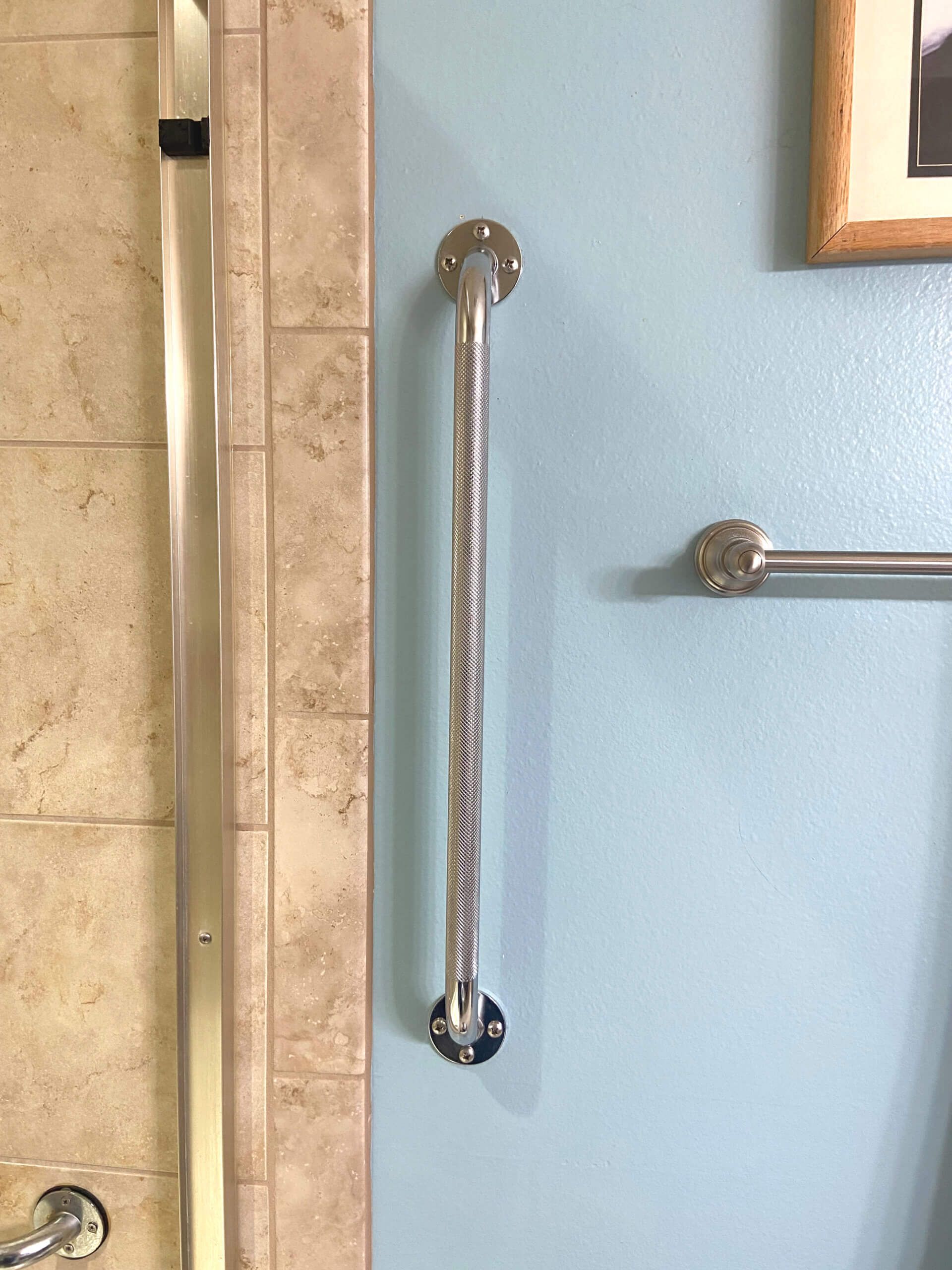 A stainless steel handle is hanging on a blue wall next to a towel rack.