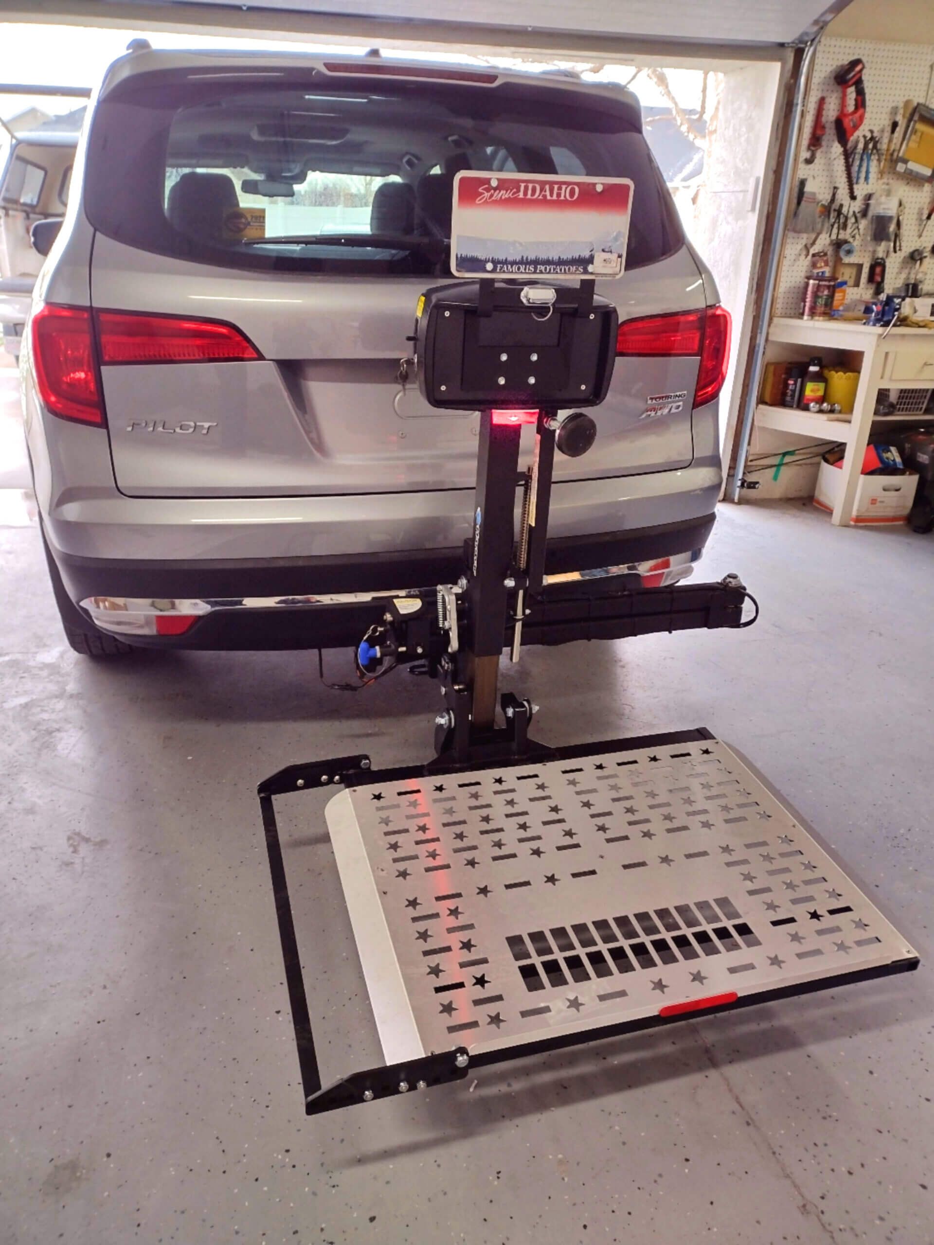 A silver SUV is parked in a garage with a lift attached to the back of it.