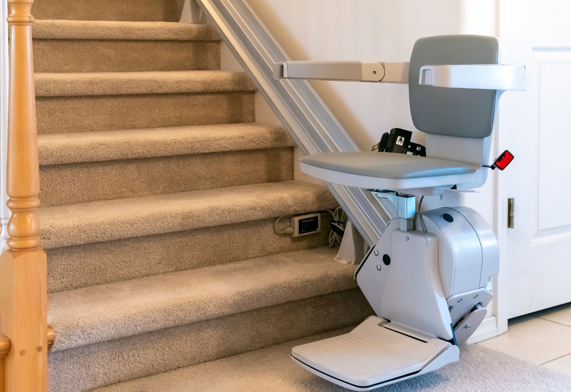 Stair lift chair installed on a carpeted staircase with a rail along the wall. Stair lift chair installed on a carpeted staircase with a rail along the wall.