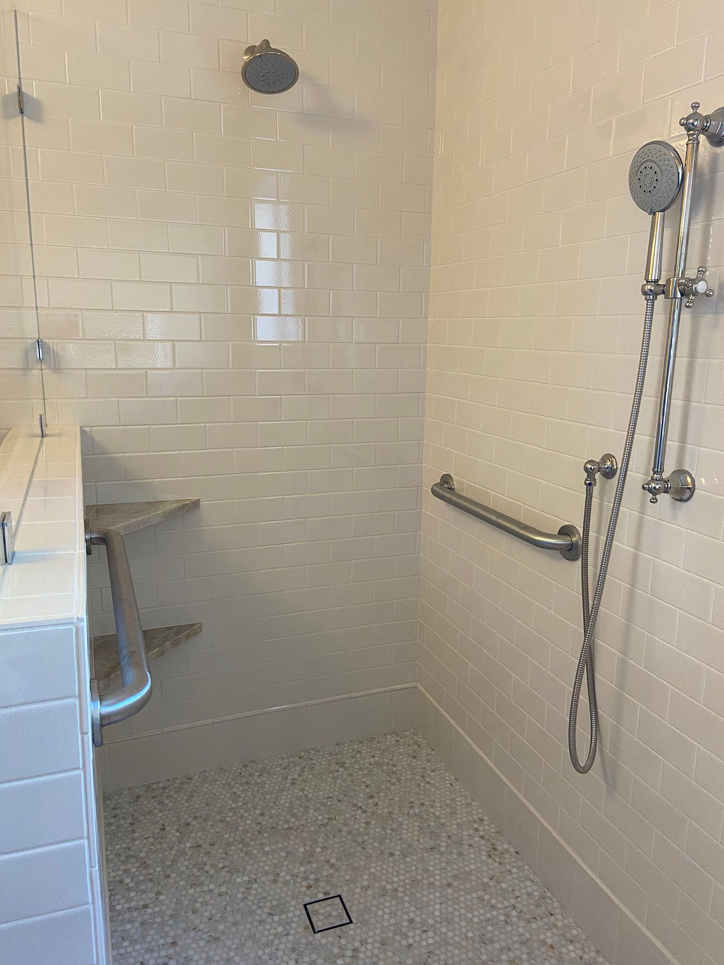 A walk in shower with a hand rail and a shower head.