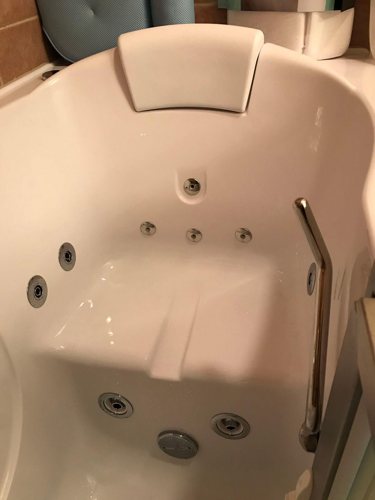 A white bathtub with jets and a headrest in a bathroom.