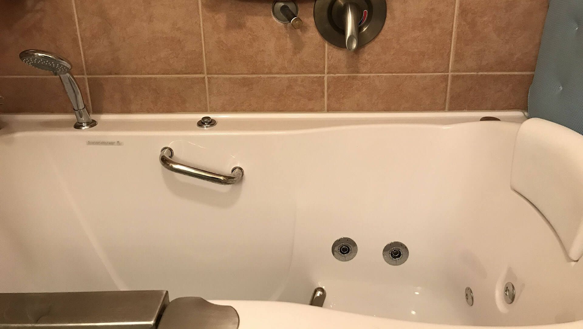 A bathtub with a handle on the side of it in a bathroom.