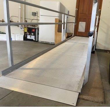 A ramp in a garage with a railing and a refrigerator in the background.