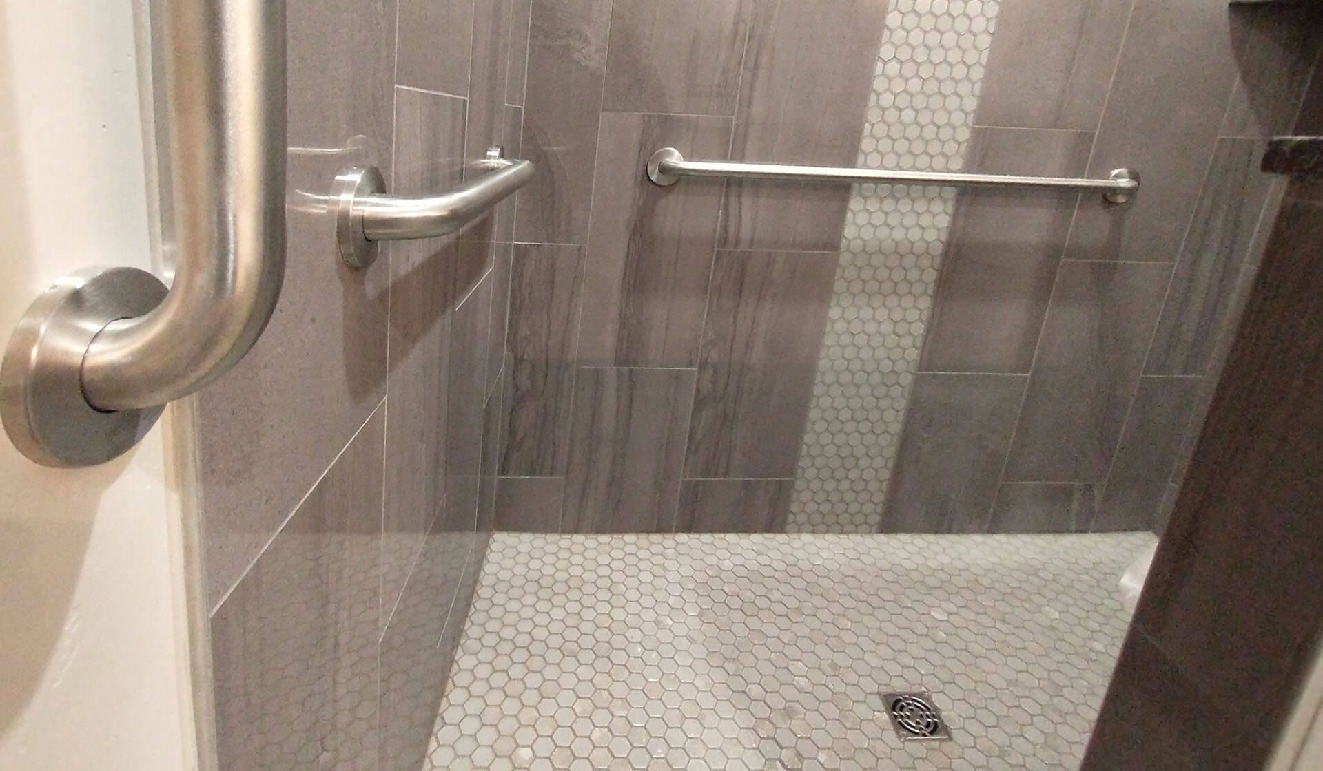 A bathroom with a walk in shower and a stainless steel hand rail.